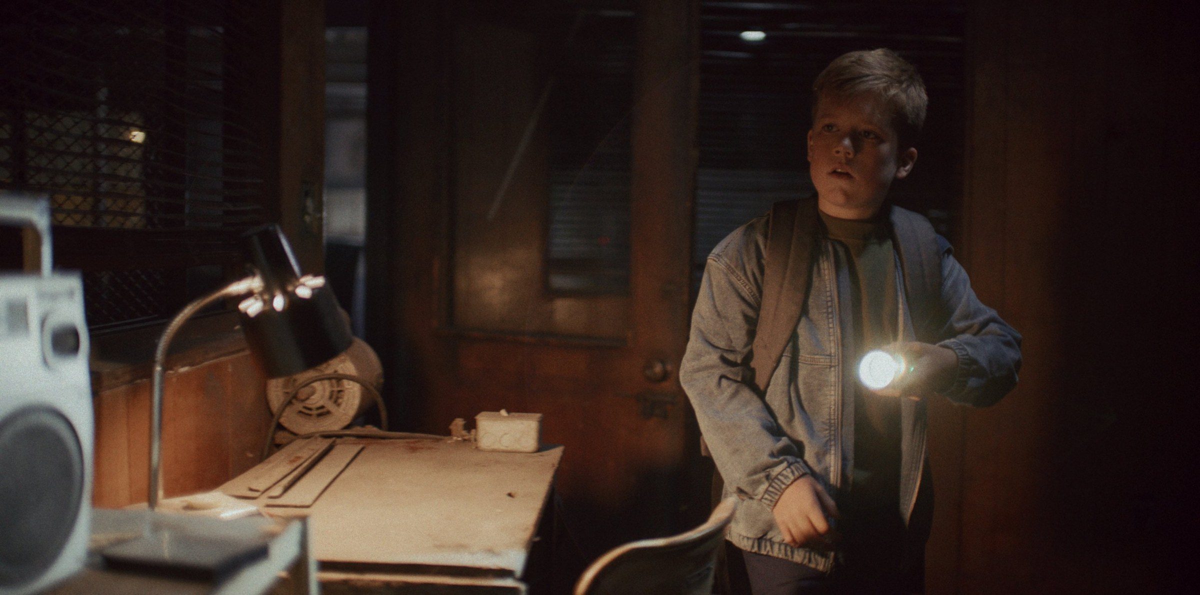 A boy with a torch beside a desk lamp in an old office