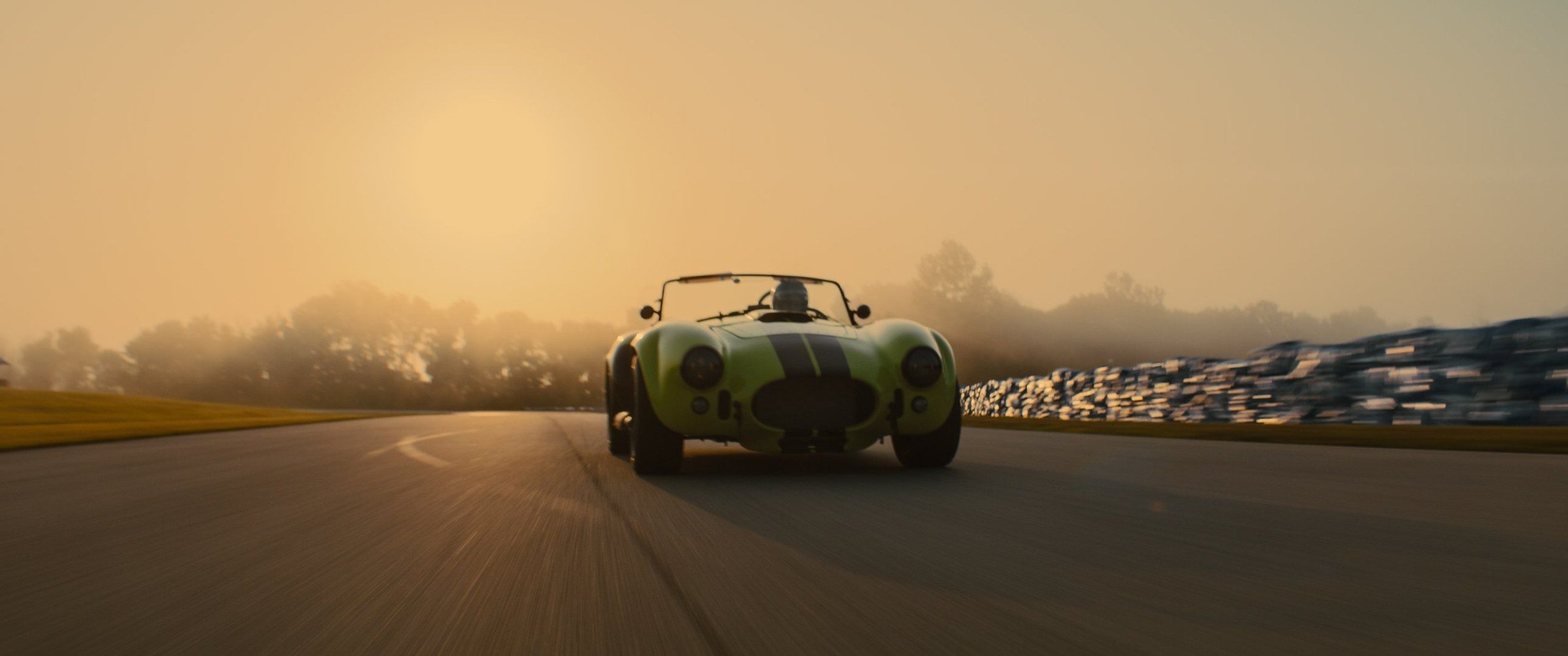 A Cobra racer coming out of golden morning haze on a racetrack
