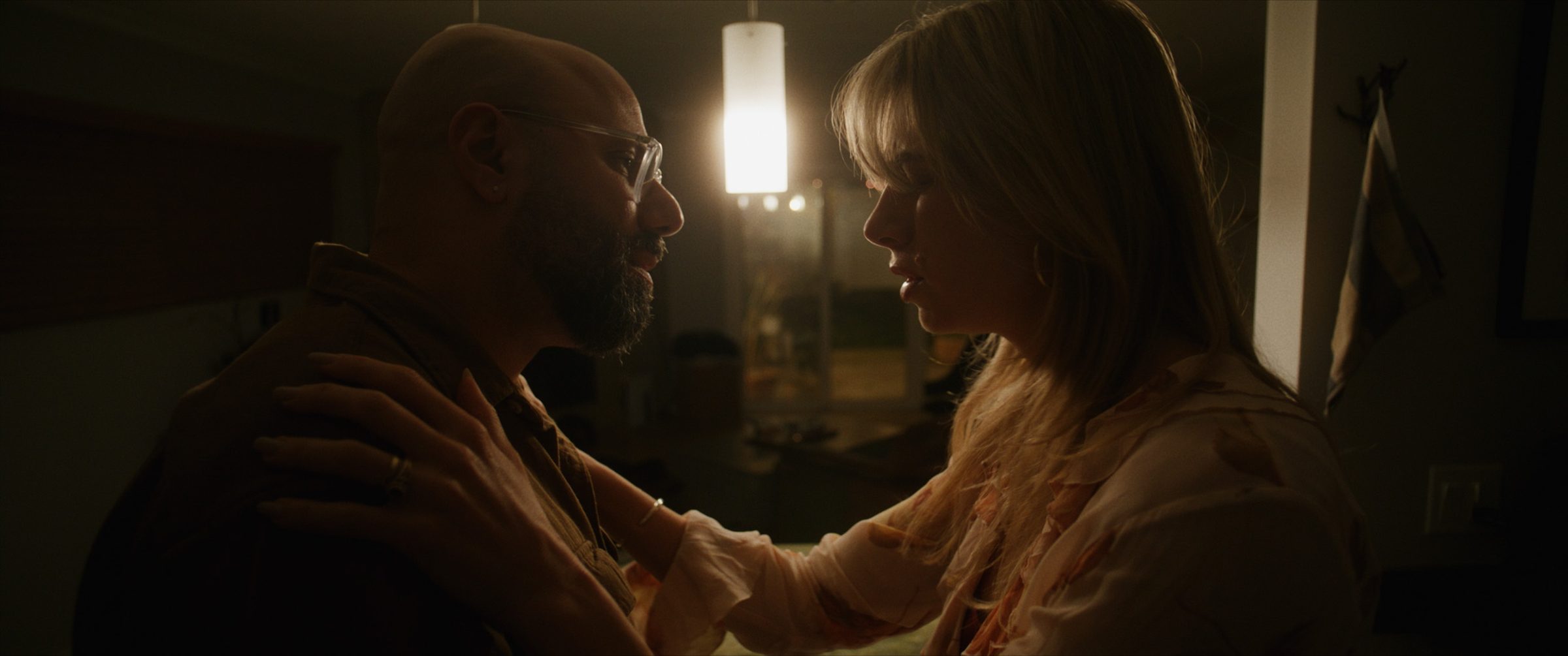 A couple in a tense embrace under a pendant light