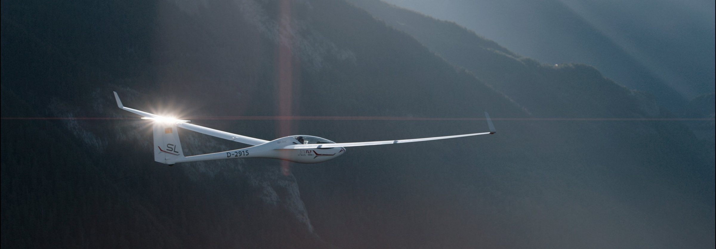 A glider banking over mountains, sun flaring off the wing