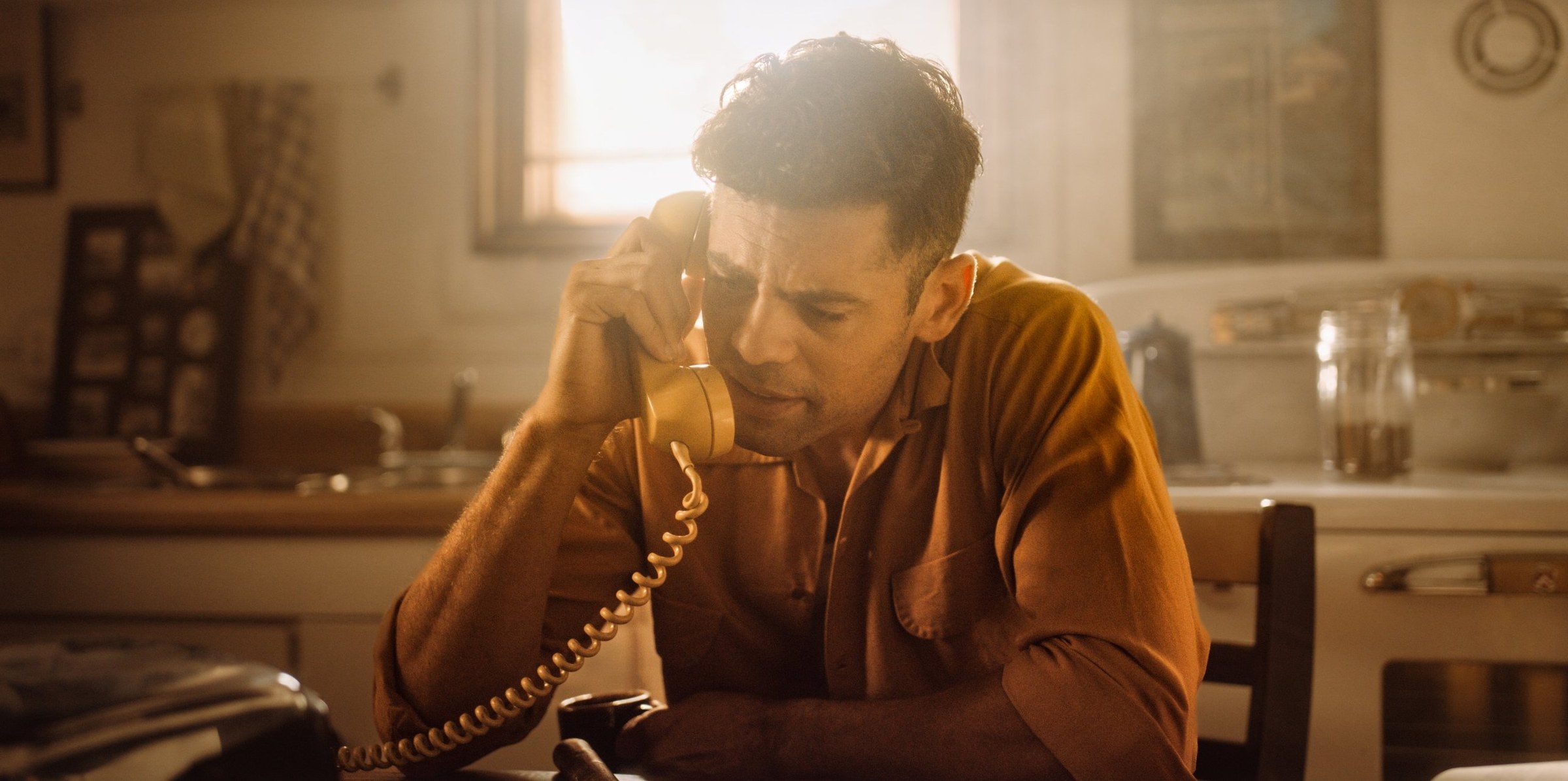 A man on a kitchen phone in warm window light