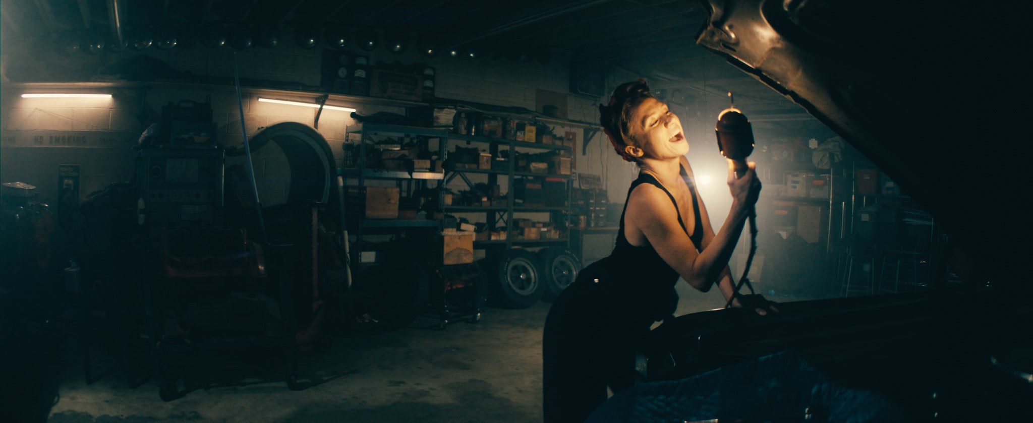 A mechanic singing into a work lamp under a raised bonnet