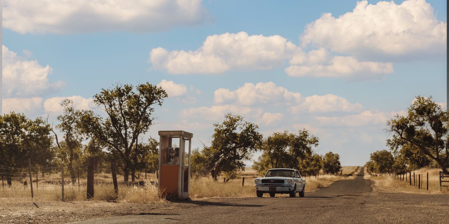 A Mustang passes a lone phone box on a dusty country road