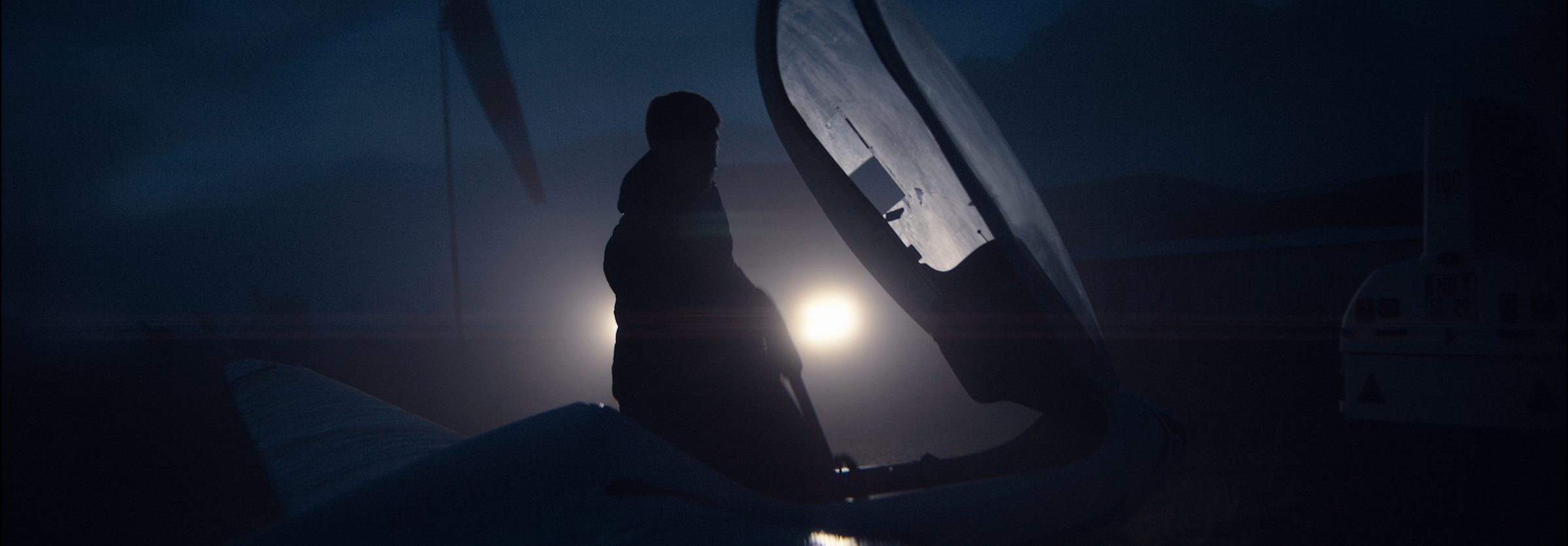 A pilot silhouetted by an open glider canopy