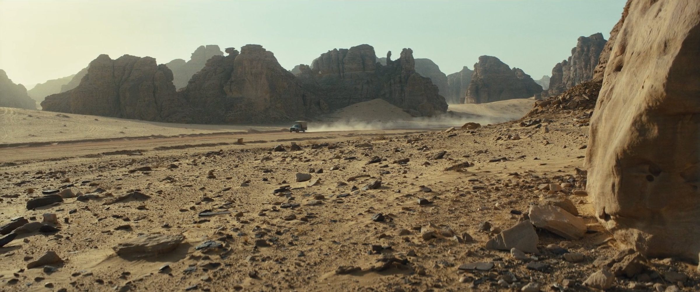 A vehicle crossing a rocky desert beneath sandstone towers