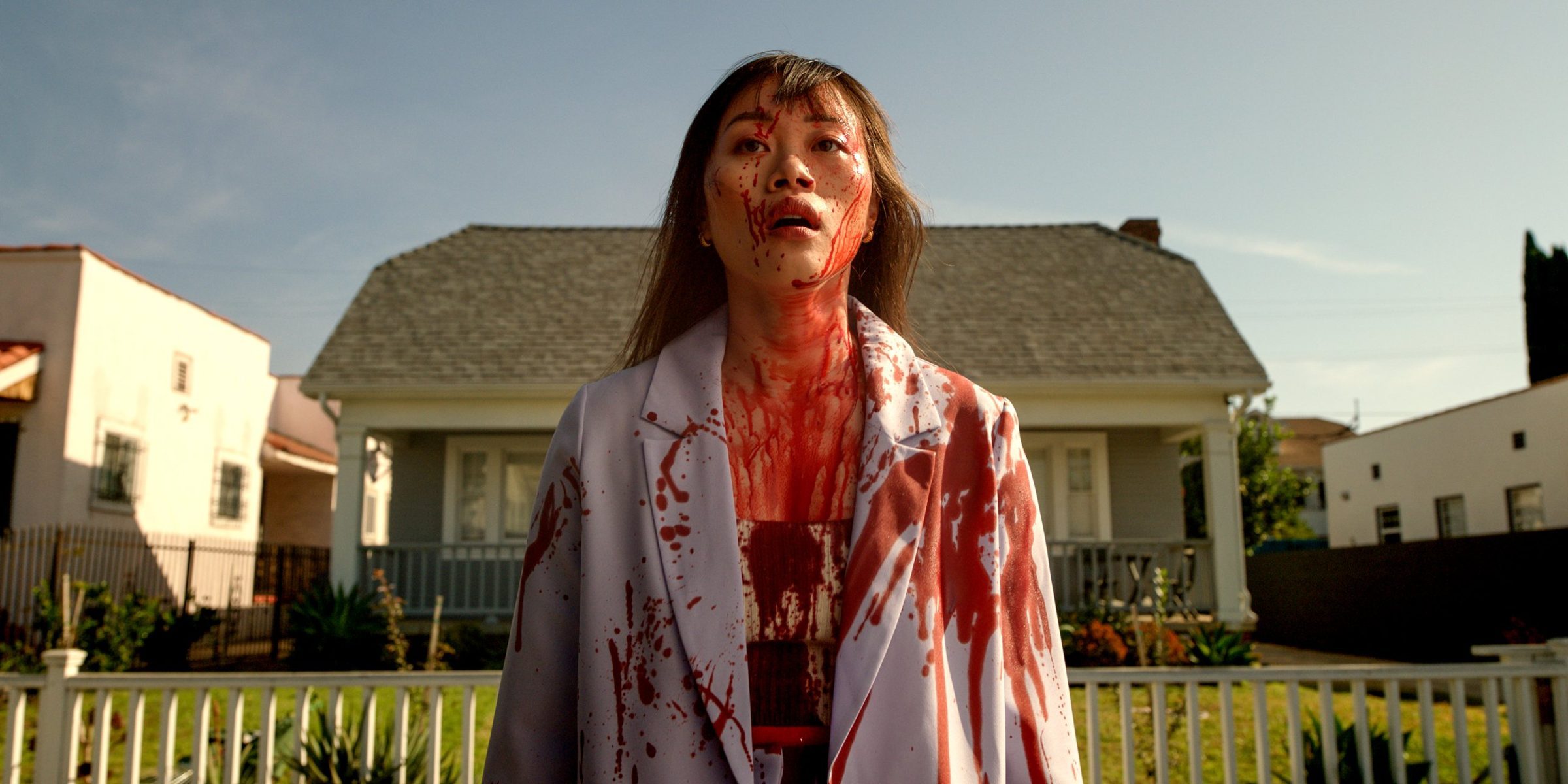 A woman in a blood-soaked dressing gown in front of her house