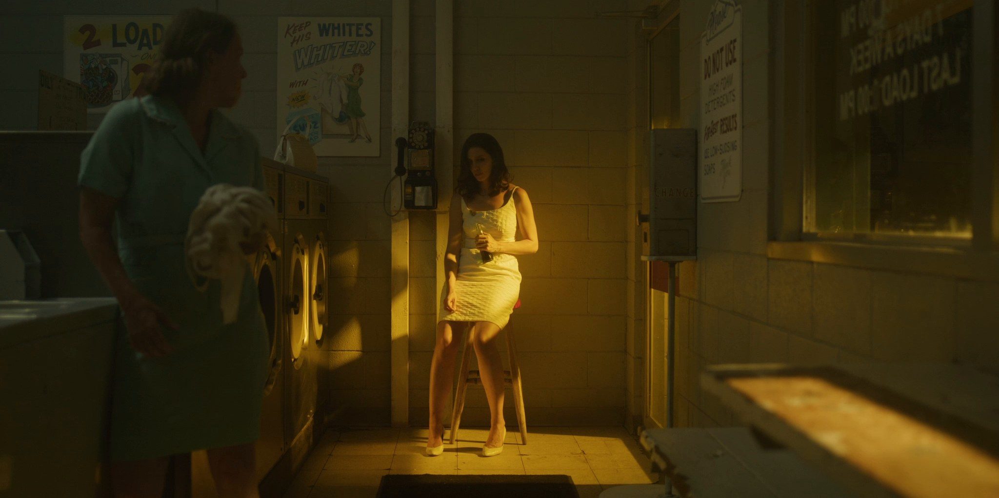A woman in a white dress sitting in a laundrette, a beam of light across her