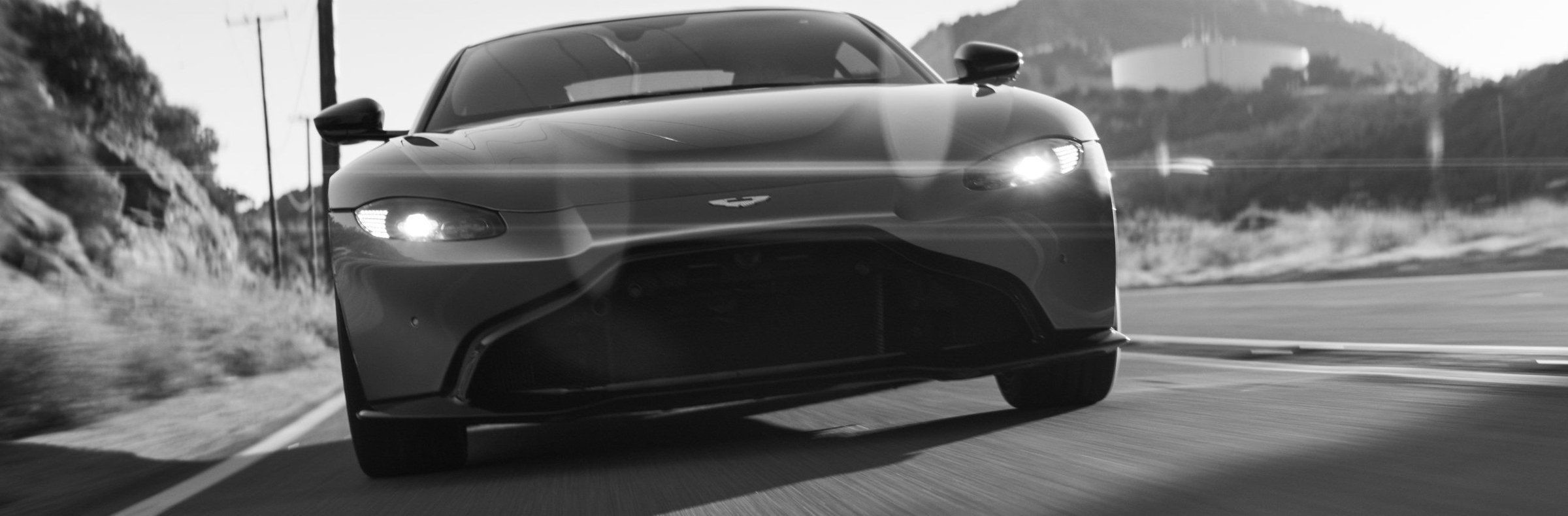 An Aston Martin head-on on a sunlit road, black and white