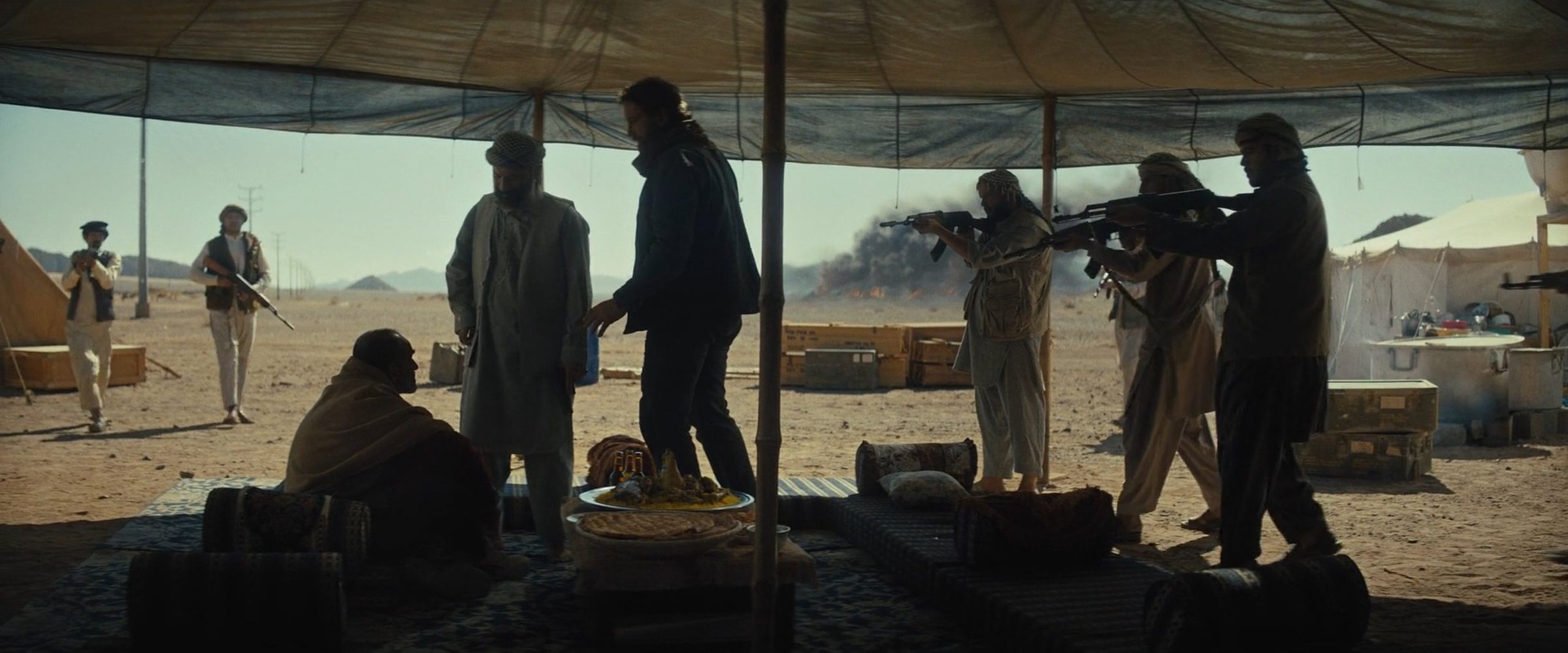 Armed men in a desert camp beneath a canopy