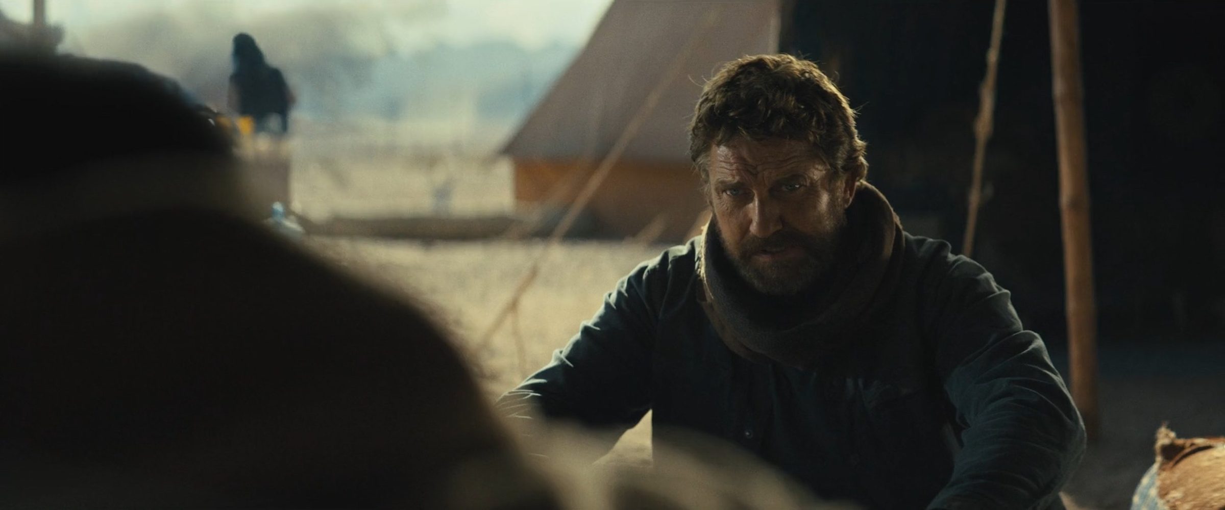 Butler crouched outside a tent, smoke on the horizon