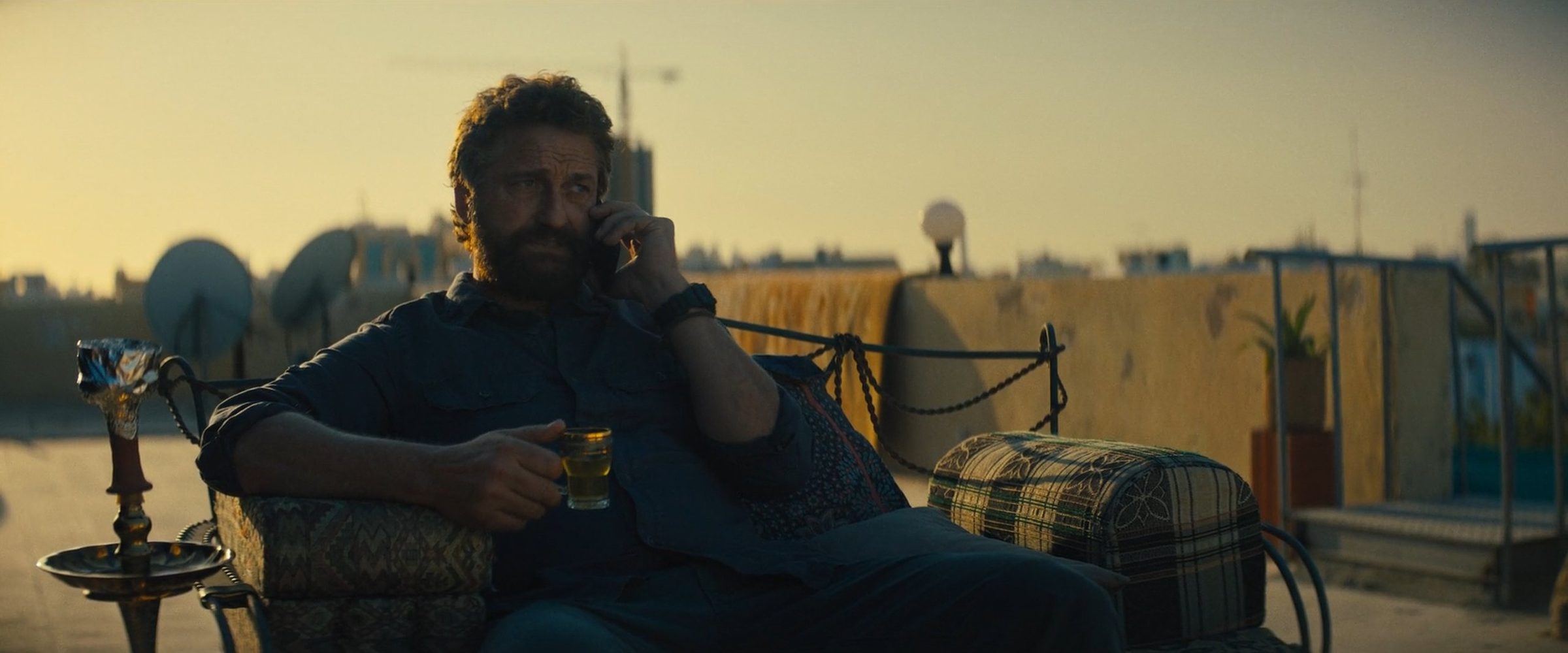 Gerard Butler on the phone on a rooftop, the city hazy behind