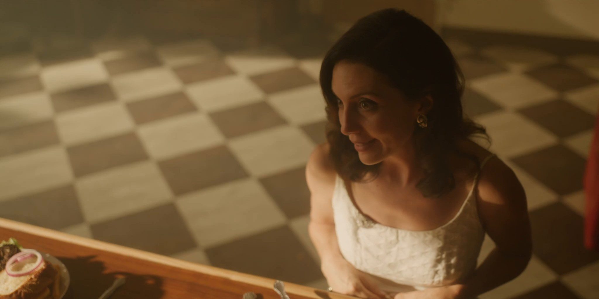 Looking down on a woman in a white dress at a diner counter, a checkered floor behind her