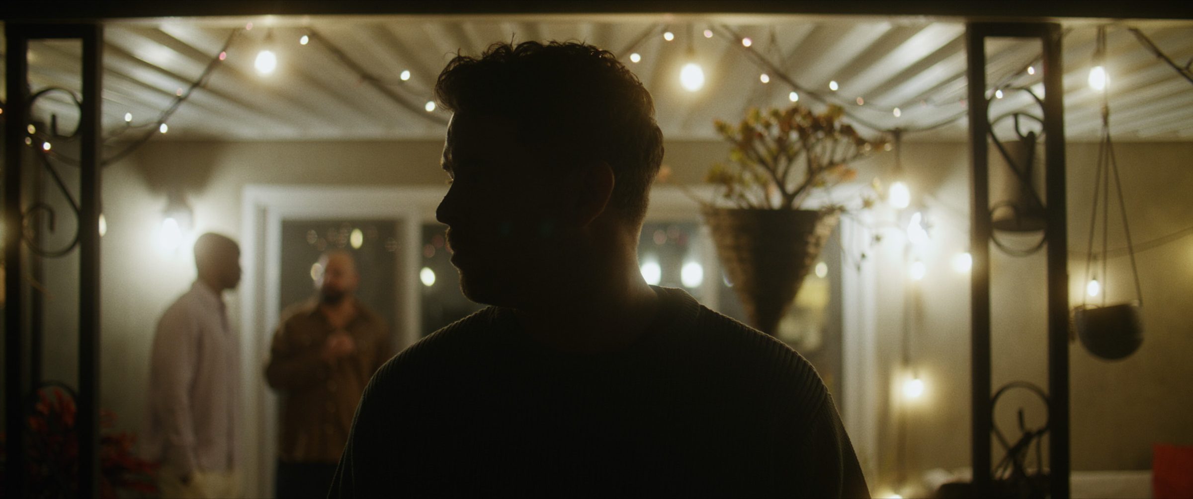 Two figures in silhouette against a wall of hanging lights
