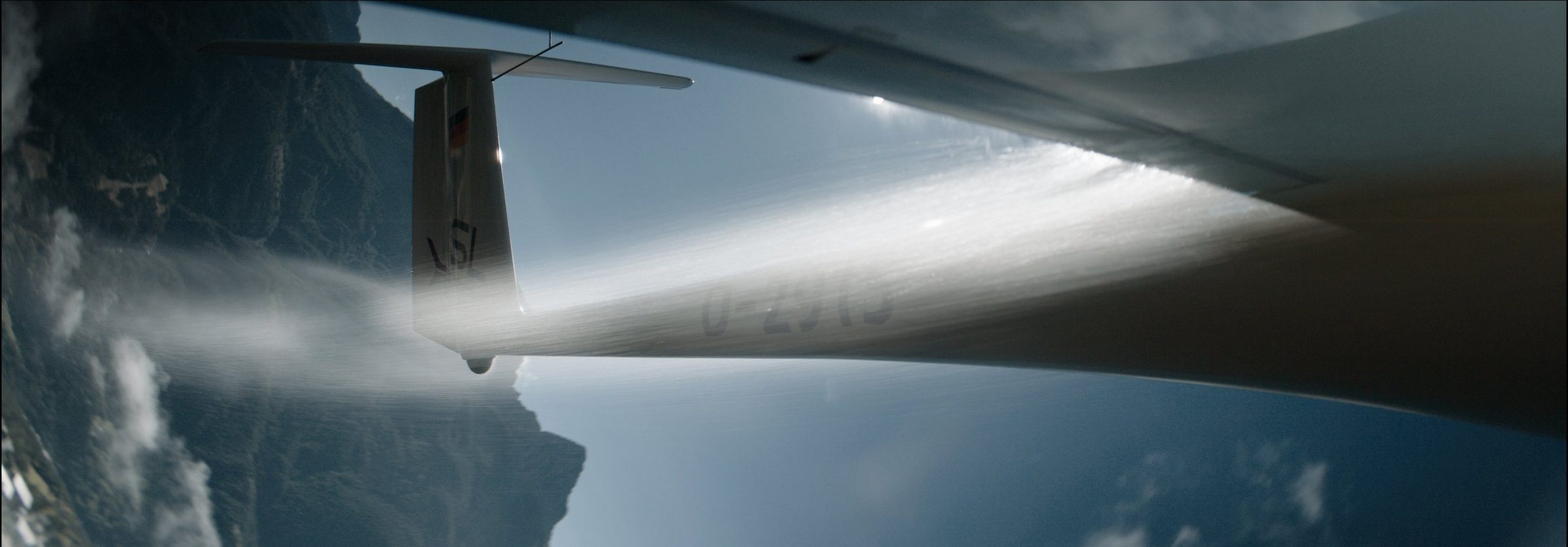Under the wing: the tail and a cloud trail against blue sky